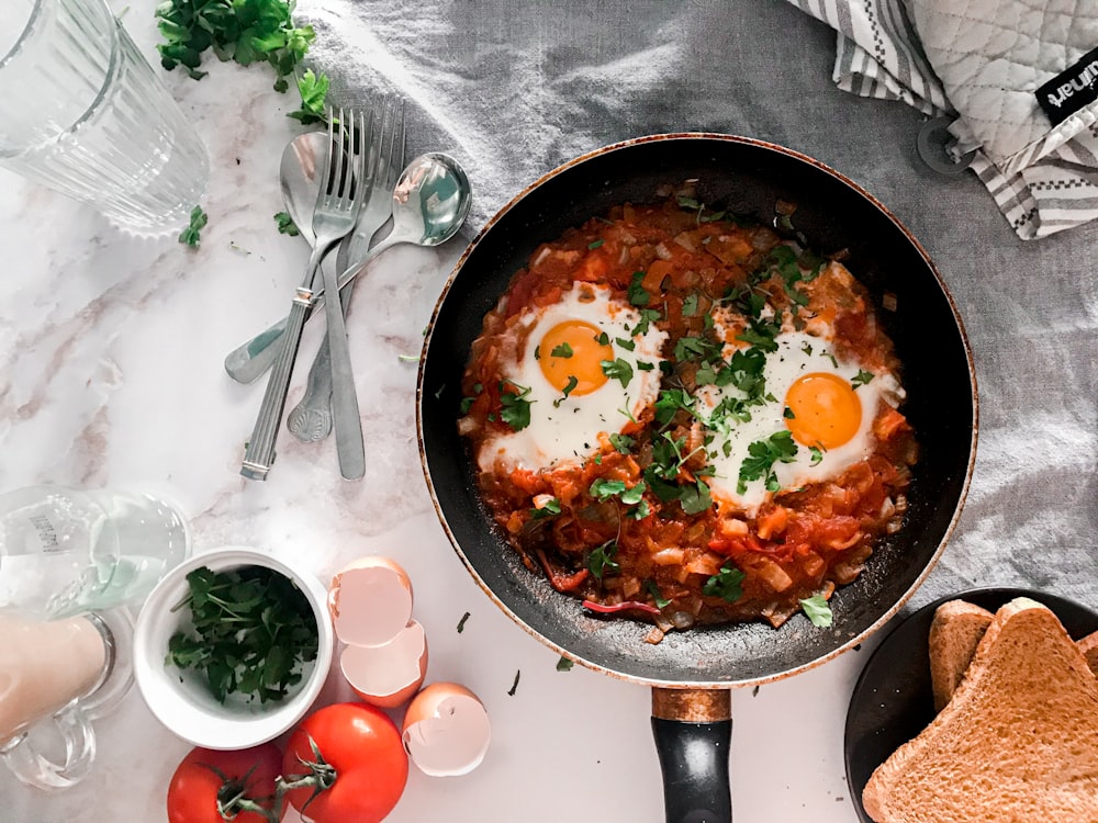 tomato soup on black cooking pan beside stainless steel fork and bread knife