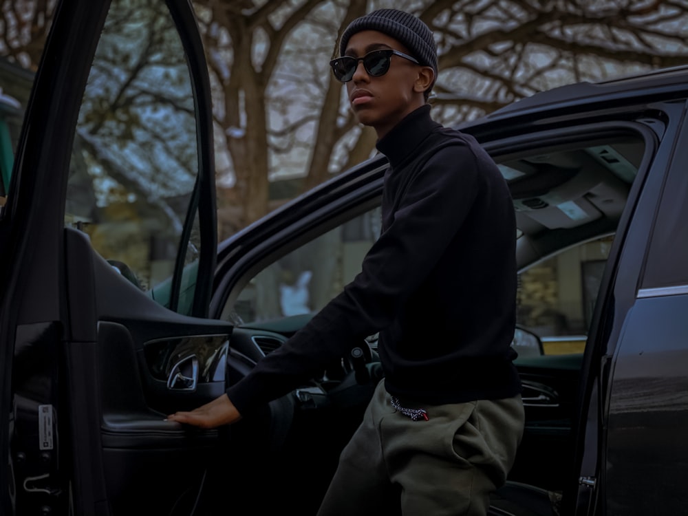 man in black jacket and brown pants sitting on black car