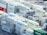 A densely packed arrangement of shipping containers, predominantly white with the word 'EVERGREEN' in green, stacked in an orderly fashion at a shipping port. The containers are on racks and appear to be refrigerated, with visible cooling units. A few containers in red, blue, and green contrast with the majority.