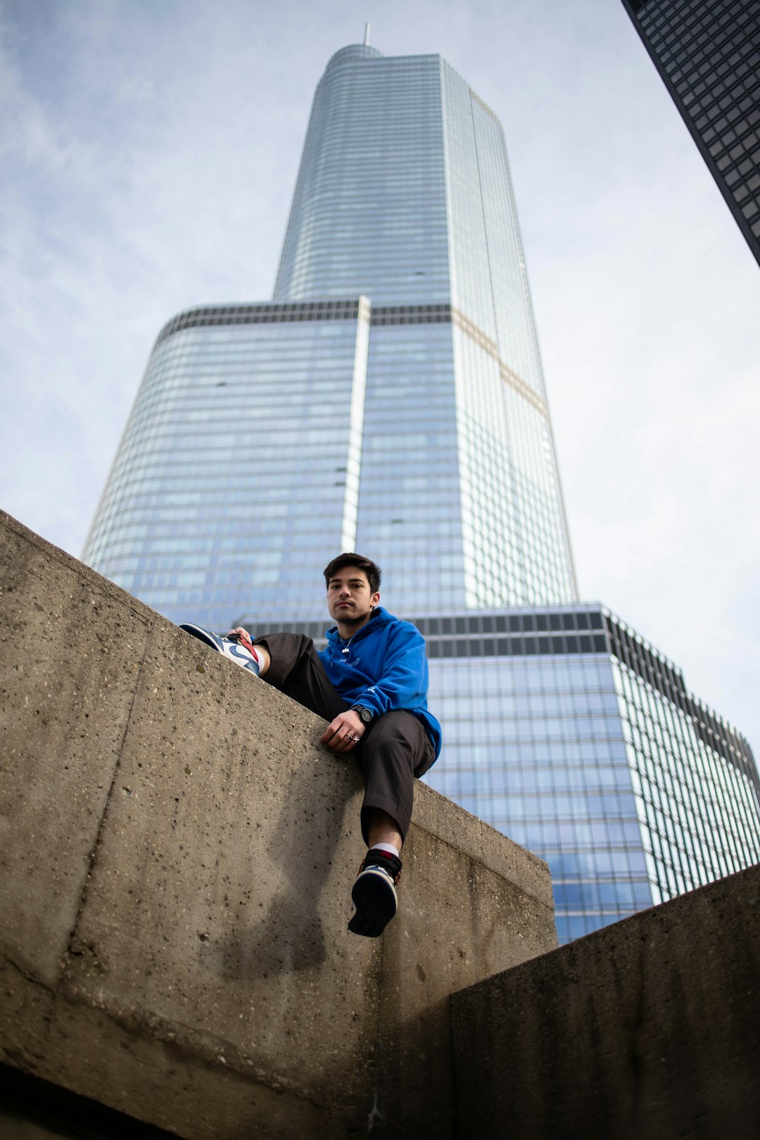 man in blue jacket sitting on concrete wall during daytime