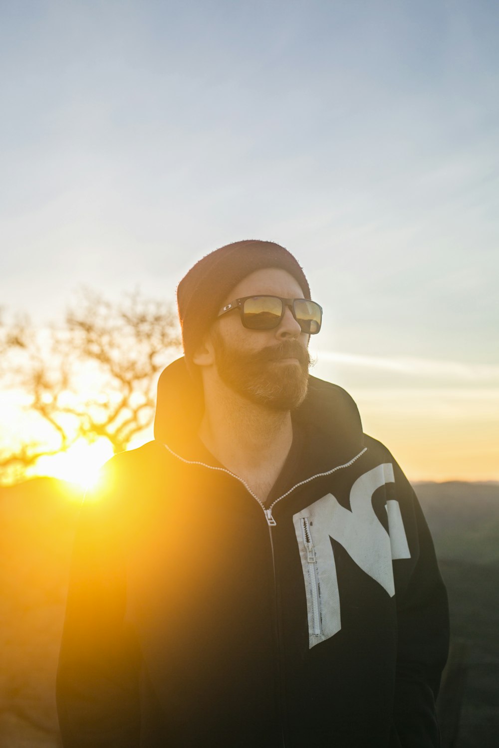 Hombre en sudadera con capucha en blanco y negro con gafas de sol negras durante la puesta de sol