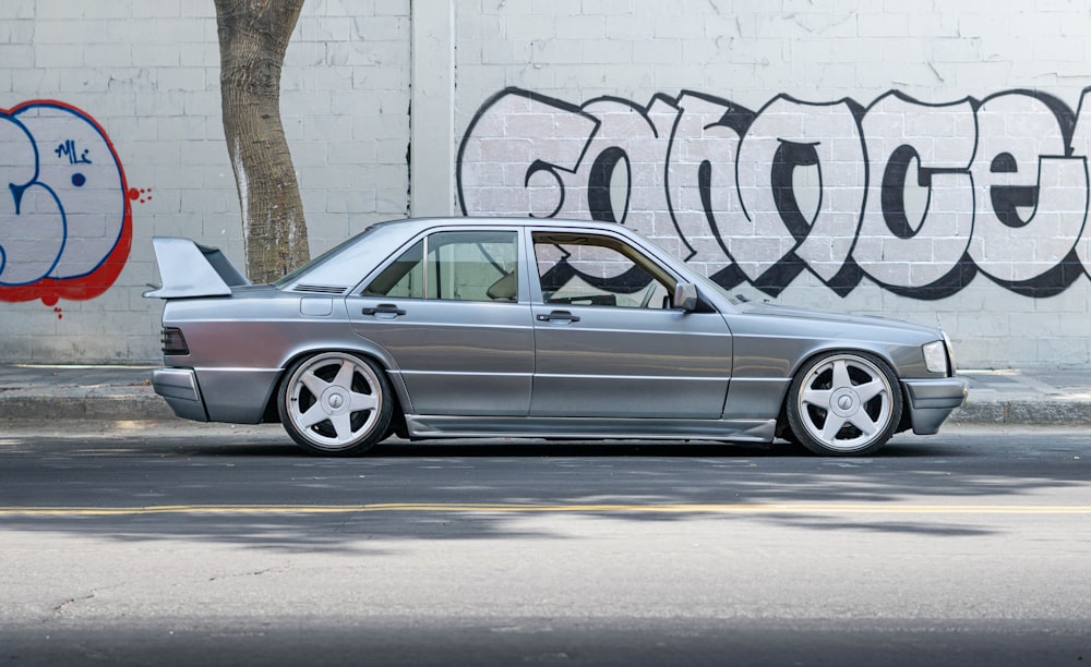 silver sedan on road beside wall with graffiti