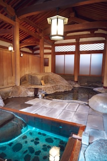 An outdoor onsen bath surrounded by natural stone and bamboo fencing, steam rising gently in the cool air