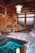 A traditional Japanese onsen bathhouse setting with wooden architecture and rock features. The interior includes a pool of clear water with visible stones at the bottom. The area is illuminated by hanging lanterns, reflecting a serene and calm ambiance. Wooden beams and frosted glass windows add to the authentic aesthetic.