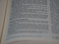 A close-up view of an open book with printed text in English. The focus is on the center of the page, with the text becoming blurred towards the edges. The text is neatly aligned in paragraphs.