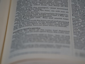 A close-up view of an open book with printed text in English. The focus is on the center of the page, with the text becoming blurred towards the edges. The text is neatly aligned in paragraphs.