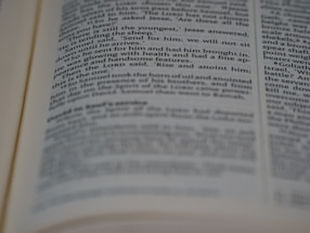 A close-up view of an open book with printed text in English. The focus is on the center of the page, with the text becoming blurred towards the edges. The text is neatly aligned in paragraphs.