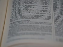 A close-up view of an open book with printed text in English. The focus is on the center of the page, with the text becoming blurred towards the edges. The text is neatly aligned in paragraphs.
