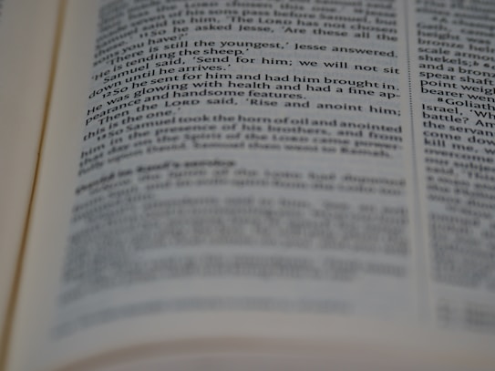 A close-up view of an open book with printed text in English. The focus is on the center of the page, with the text becoming blurred towards the edges. The text is neatly aligned in paragraphs.