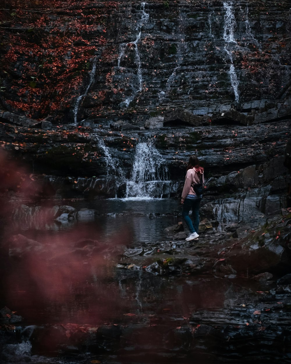 黒いジャケットとブルーデニムジーンズの男が滝の前の岩の上に立つ