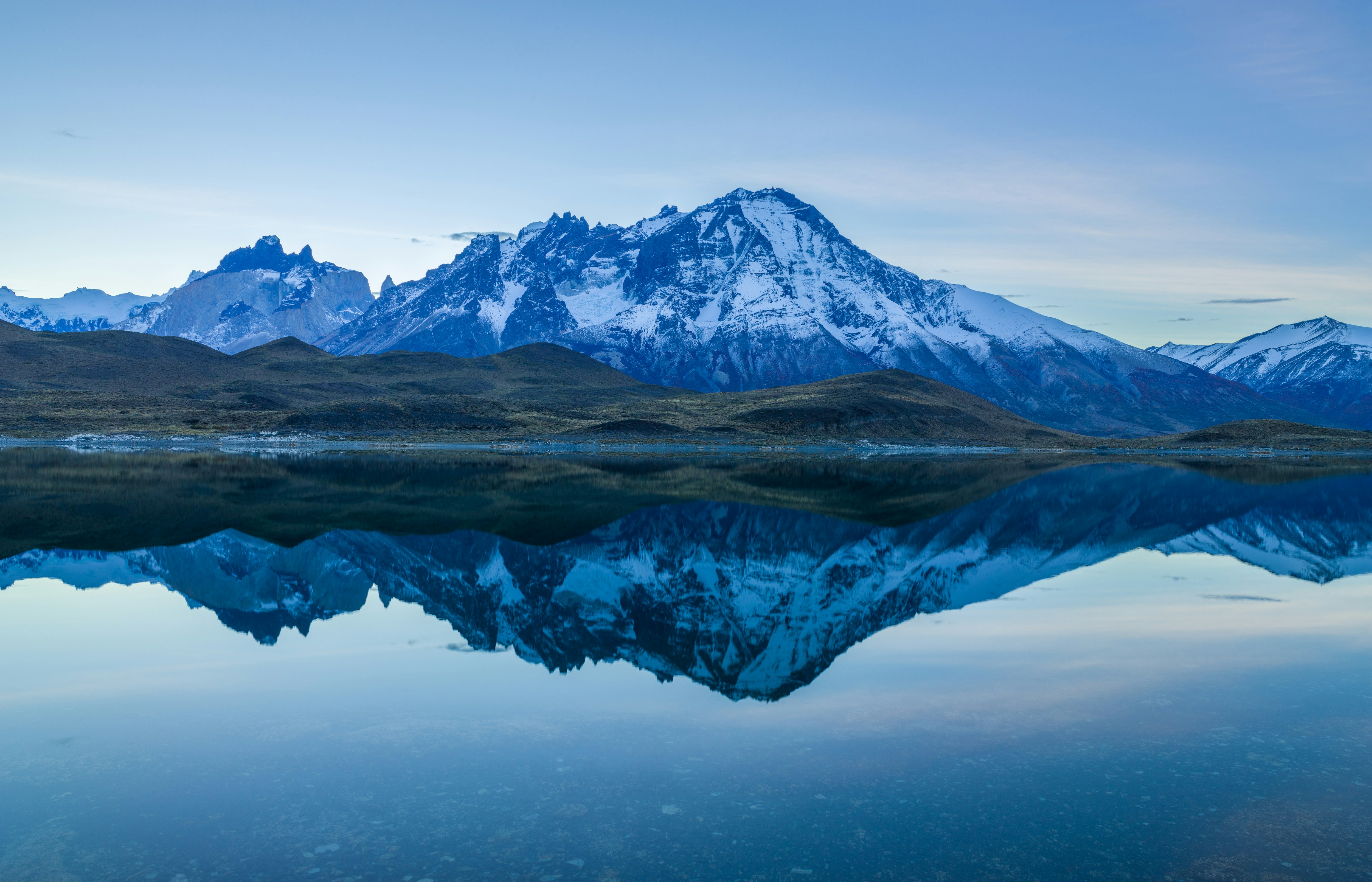snow covered mountain near body of water during daytime, Paine mountain range reflects in a lake before sunrise