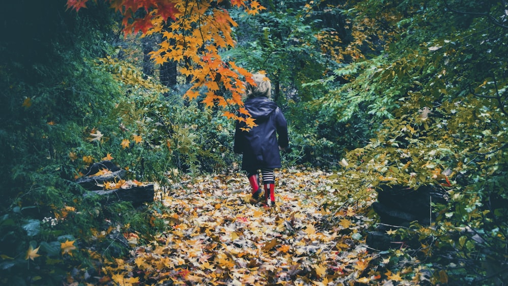 黒いジャケットと赤いズボンを着た女性が、地面の枯れ葉の上を歩いている