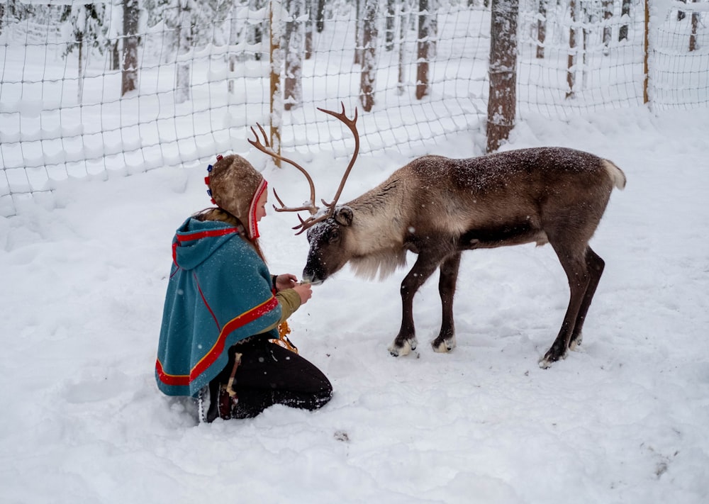 woman in red coat and black pants sitting on snow covered ground beside black and brown