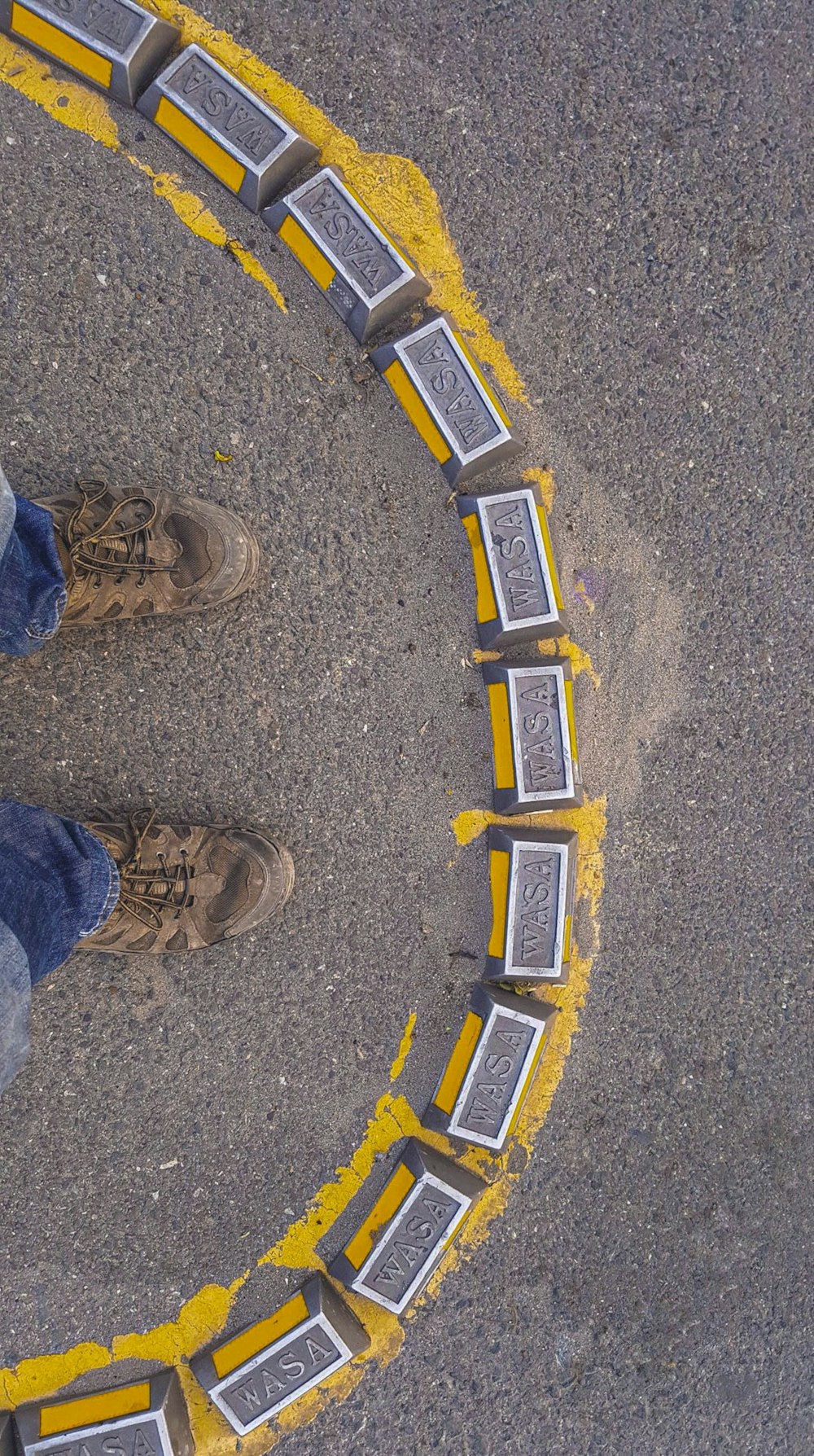 person wearing blue denim jeans and brown hiking shoes standing on gray concrete floor