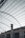 The image features a structure with an expansive metal framework, resembling an industrial or warehouse setting. The roof is open, revealing a network of beams and wires. Below, there is an old, weathered building with rusted metal bars and a tall chimney protruding through the roof.