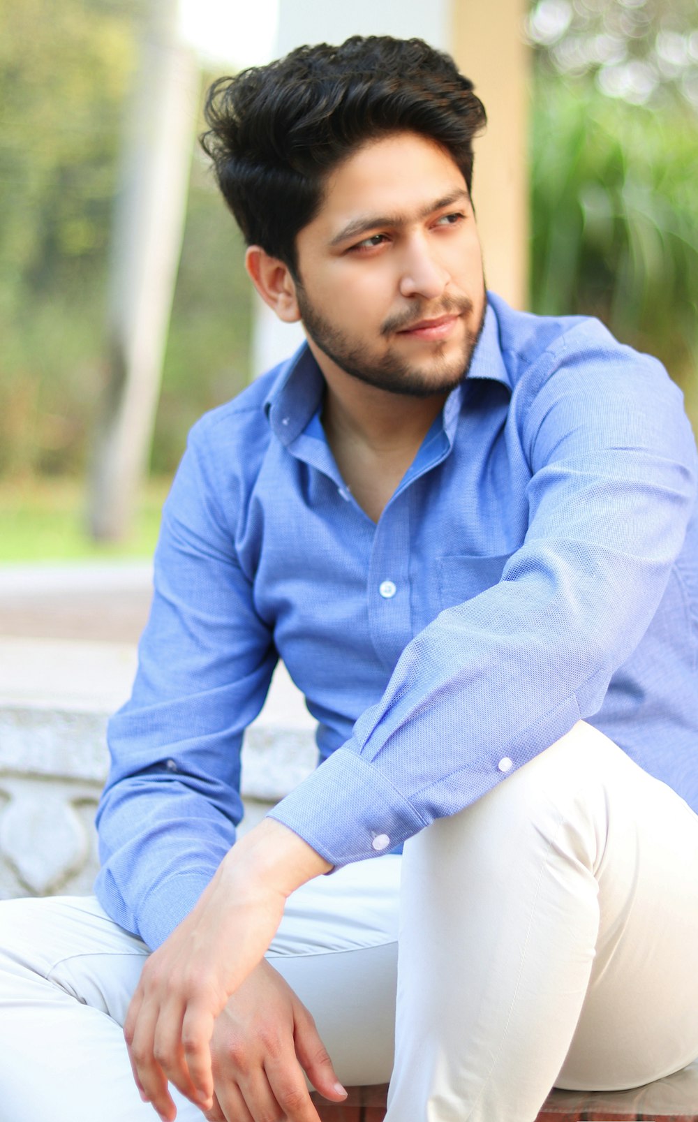 man in blue dress shirt and white pants sitting on concrete bench during daytime