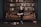 A young person sits on a brown leather couch in a library, surrounded by books. The bookshelf behind is filled with various books, and some books are scattered on the floor. The setting has a classic and cozy library feel.