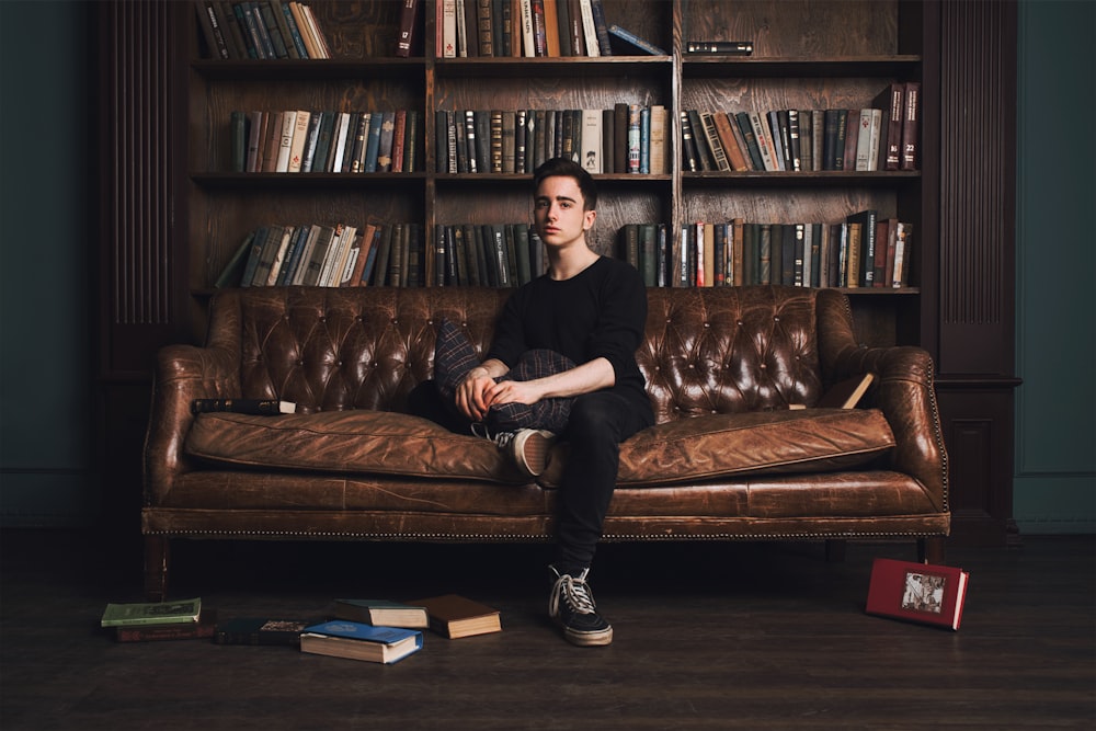 man in black long sleeve shirt sitting on brown leather couch