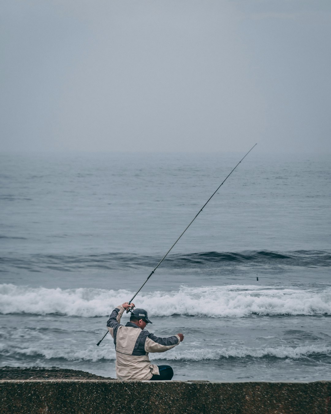 man in red and black jacket and black pants fishing on sea during daytime