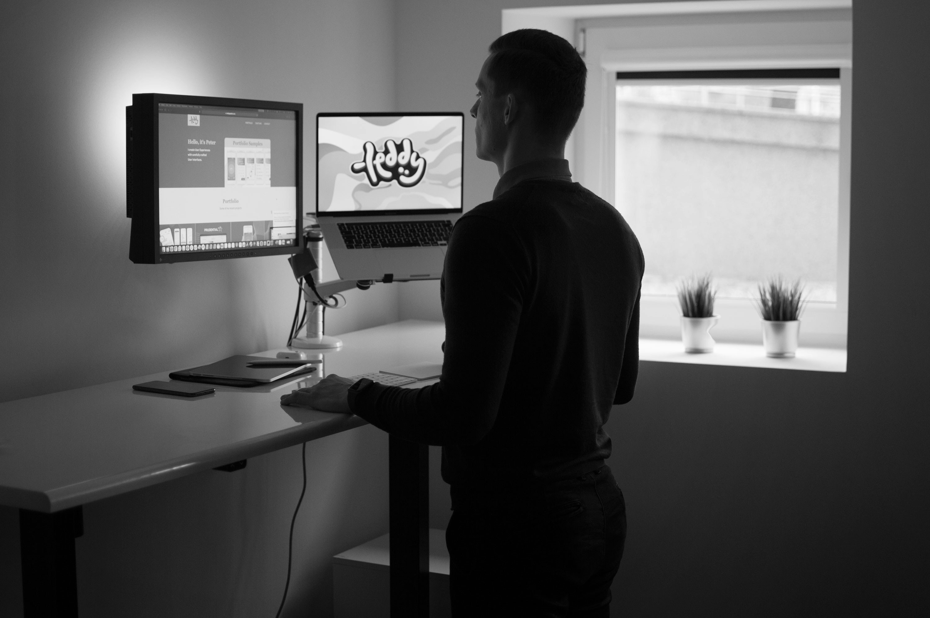 a Man standing by his desk with two monitors