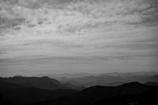 Black and white landscape showing misty mountains under a cloudy sky.