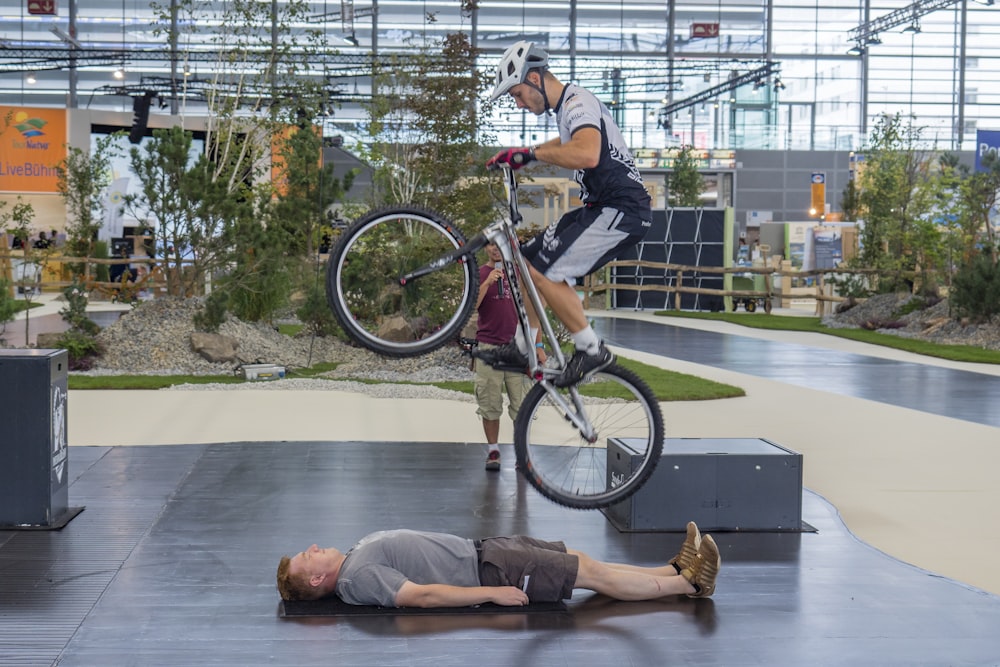 man in gray t-shirt and black shorts lying on floor beside black and red bicycle