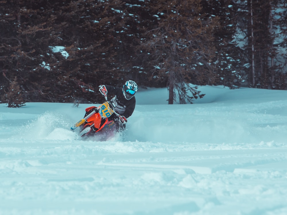 person in black jacket riding orange snow sled on snow covered ground during daytime