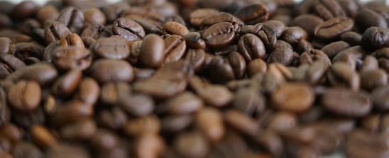 Close-up of glossy coffee beans resting on a sleek black matte surface with golden highlights.