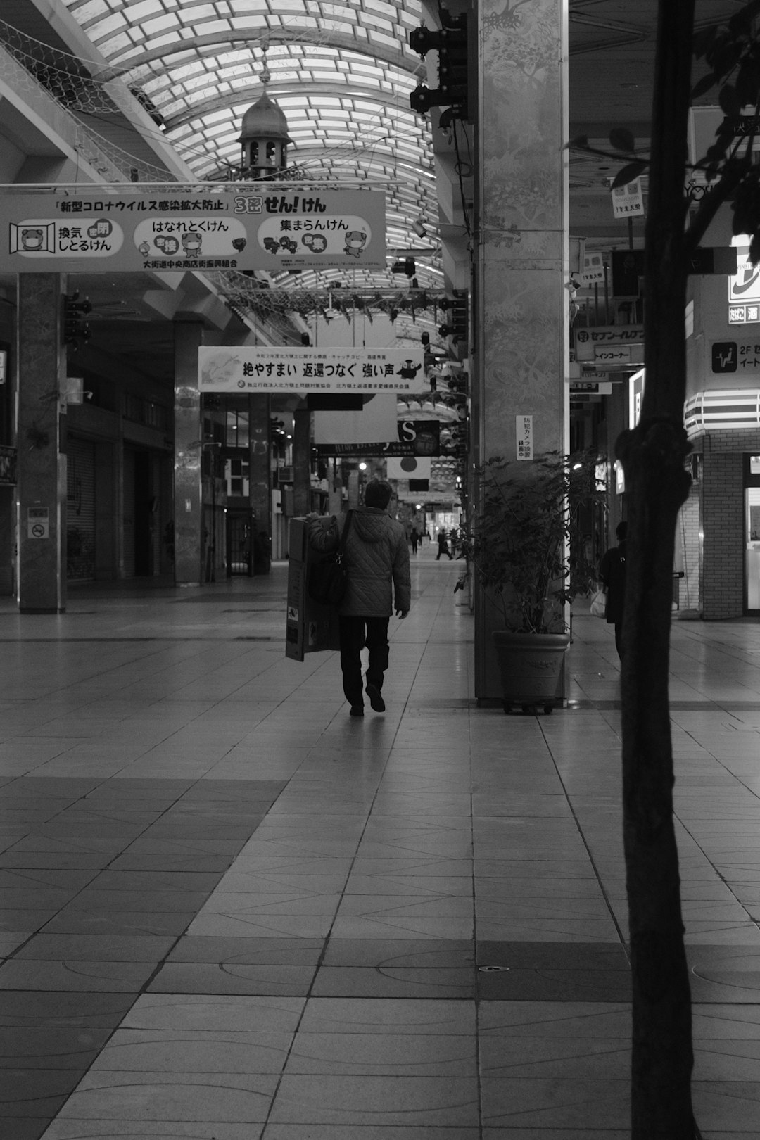 grayscale photo of man walking on sidewalk