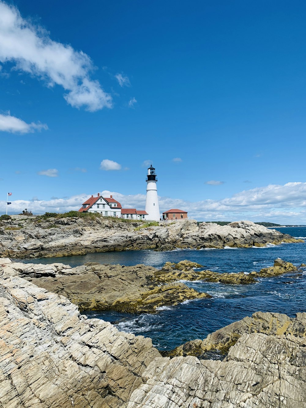 white and red lighthouse on rocky shore under blue sky during daytime
