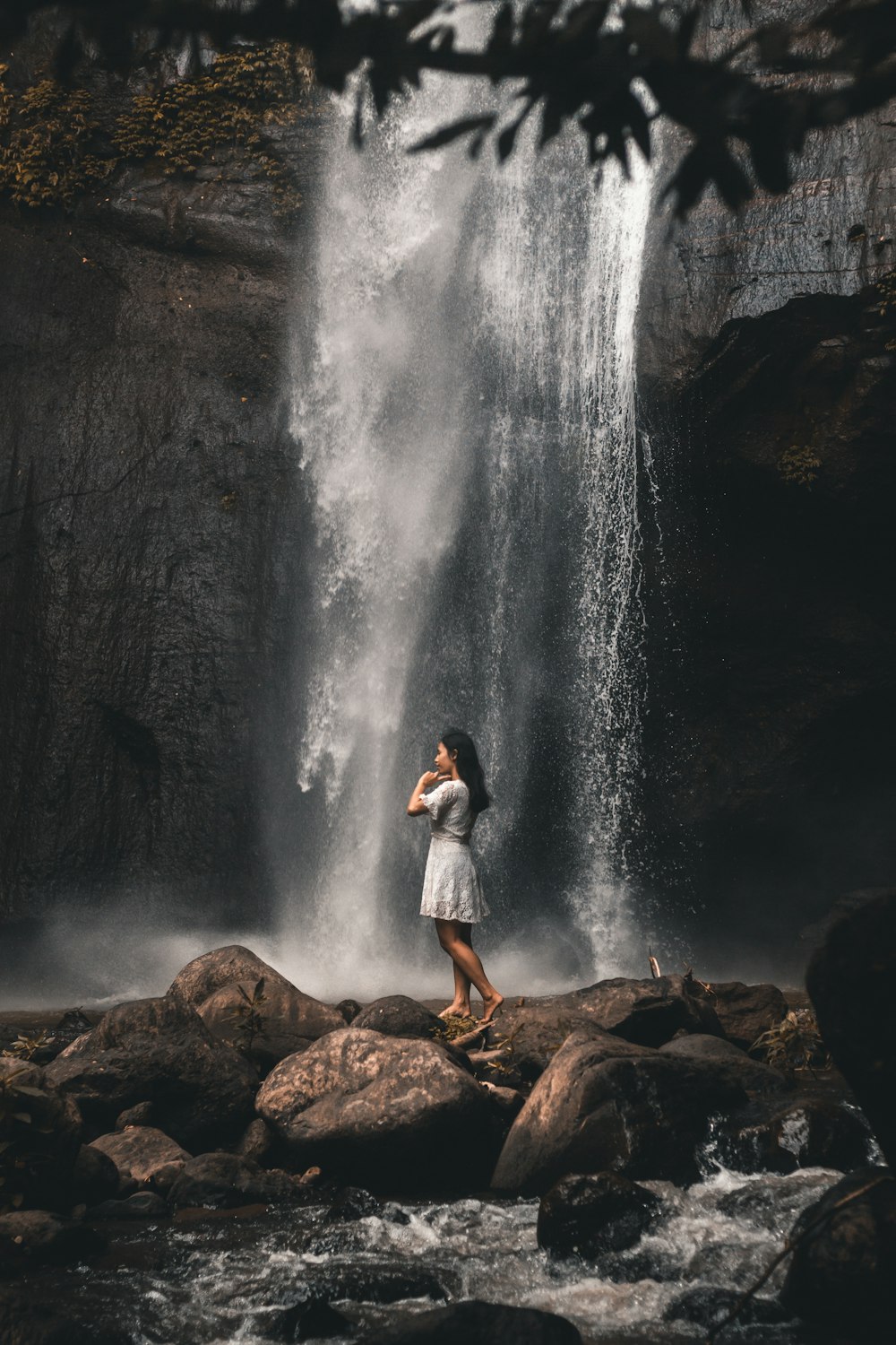 man in blue denim jacket standing on brown rock near waterfalls during daytime