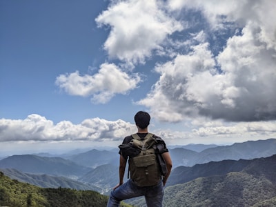 A scenic mountain peak with a backpacker standing at the summit, overlooking the valley below.