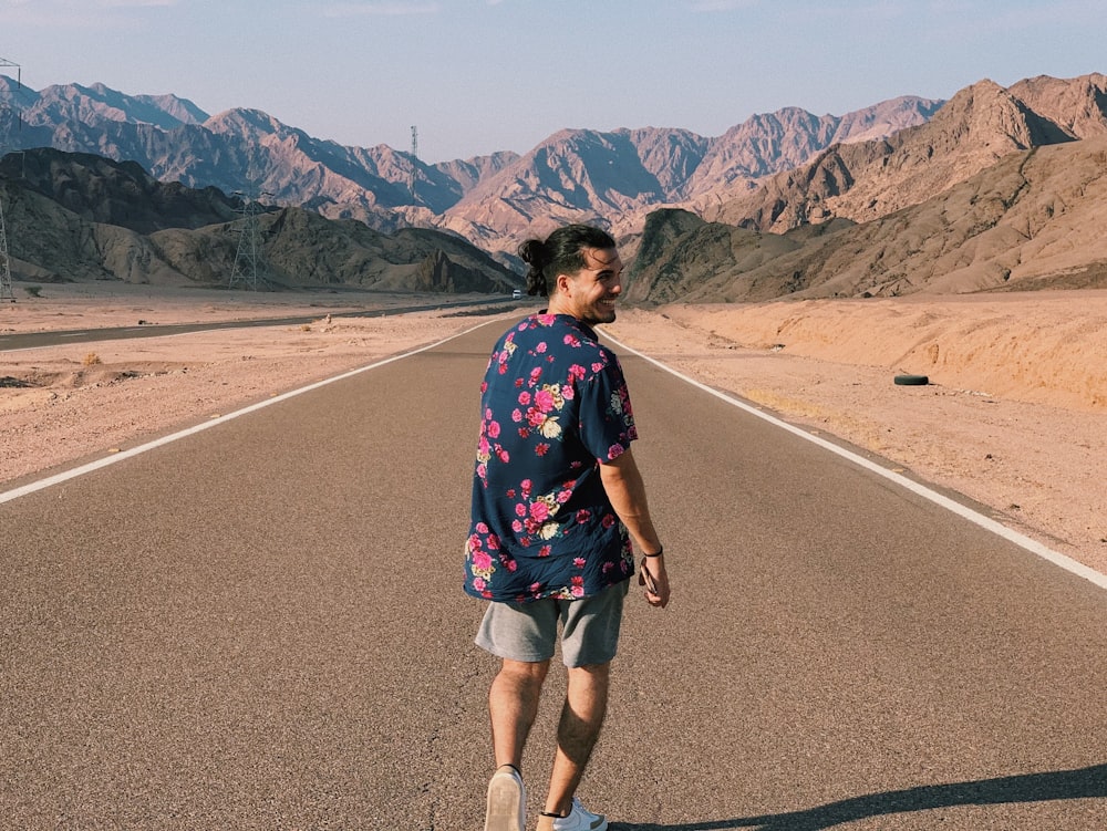 woman in black and pink floral shirt standing on gray asphalt road during daytime