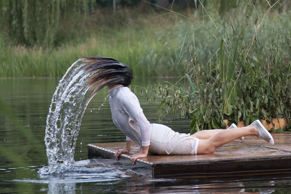 woman in white long sleeve shirt and white pants sitting on brown wooden dock near water