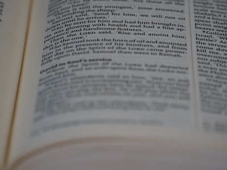 A close-up view of an open book showing printed text in English. The text is in two columns, with portions of it slightly out of focus due to the depth of field.