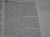 A close-up view of a page from a book with text that includes an account from the Bible. The focus is on the left side of the page, with text in columns, while the right side is slightly out of focus, showing lined paper with handwritten notes.