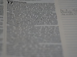 A close-up view of a page from a book with text that includes an account from the Bible. The focus is on the left side of the page, with text in columns, while the right side is slightly out of focus, showing lined paper with handwritten notes.