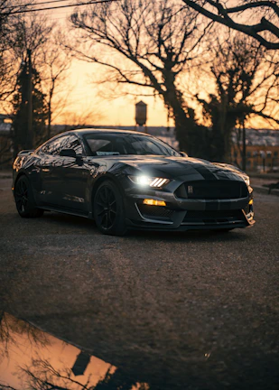 Sleek black sports car parked under city lights at dusk.