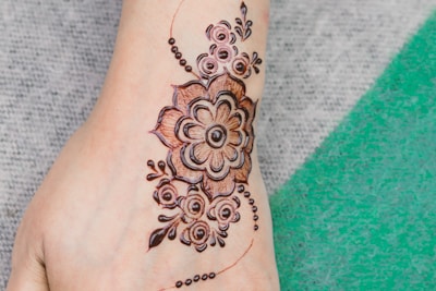 Intricate henna design displayed on a foot. The artwork features a floral pattern with geometric elements and swirling motifs, blending traditional and contemporary styles.