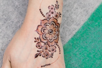 Intricate henna design displayed on a foot. The artwork features a floral pattern with geometric elements and swirling motifs, blending traditional and contemporary styles.
