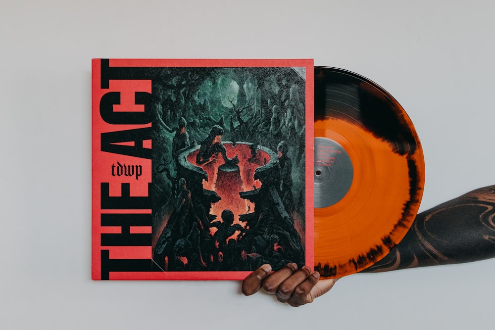 a hand holding an orange and black vinyl album