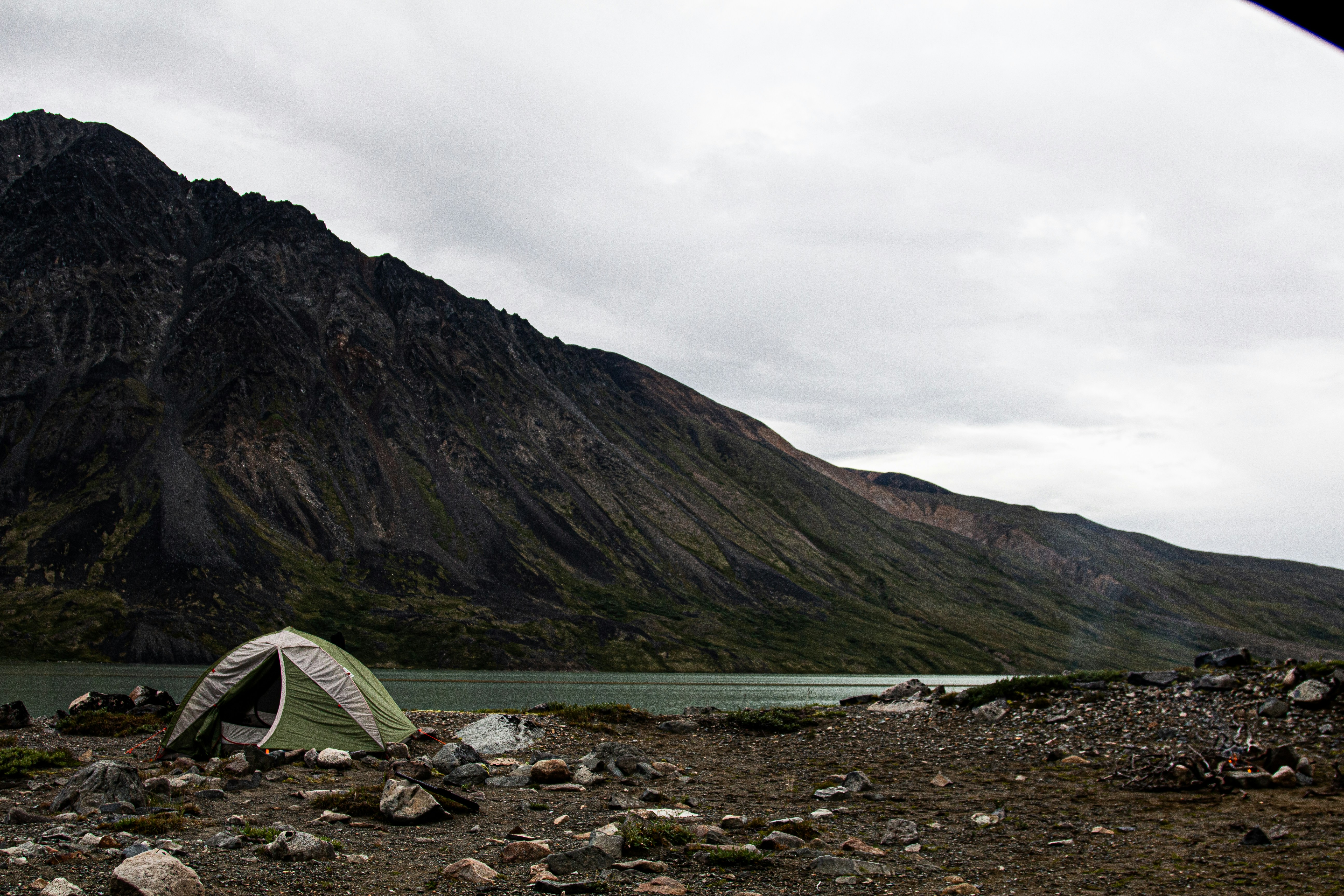green tent on rocky shore near mountain under cloudy sky during daytime