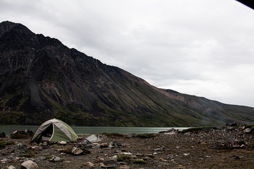 green tent on rocky shore near mountain under cloudy sky during daytime