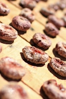 Rows of dried figs are arranged on a wooden surface, capturing the natural textures and earthy colors. The figs have a dehydrated appearance with some red hues visible in the center.