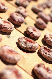 Rows of dried figs are arranged on a wooden surface, capturing the natural textures and earthy colors. The figs have a dehydrated appearance with some red hues visible in the center.