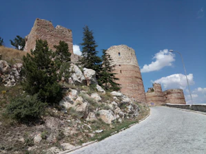 A winding hiking trail through lush green hills near a medieval fortress.