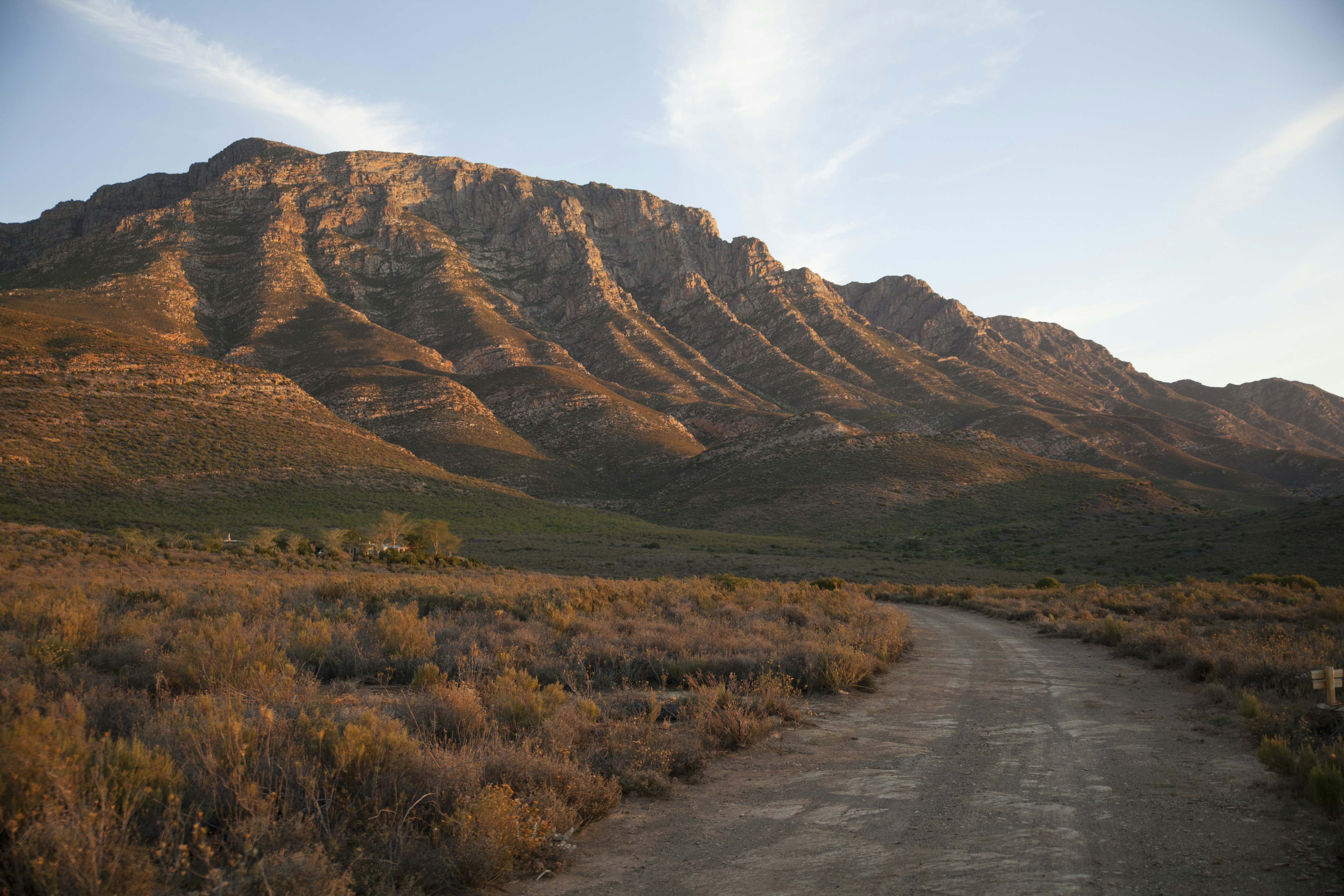 brown and green grass field near brown mountain under white clouds during daytime