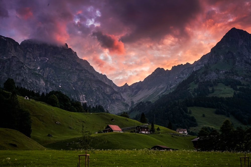 green grass field near mountain under cloudy sky during daytime