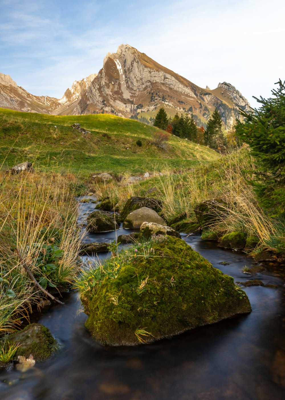 green grass and brown rocky mountain beside river during daytime
