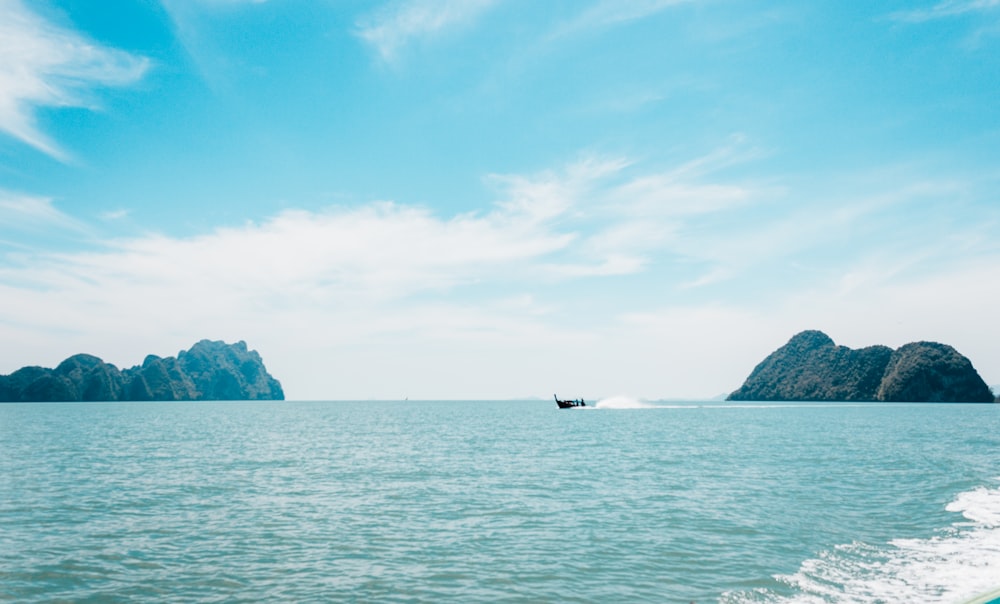 boat sailing on sea near island under blue sky during daytime